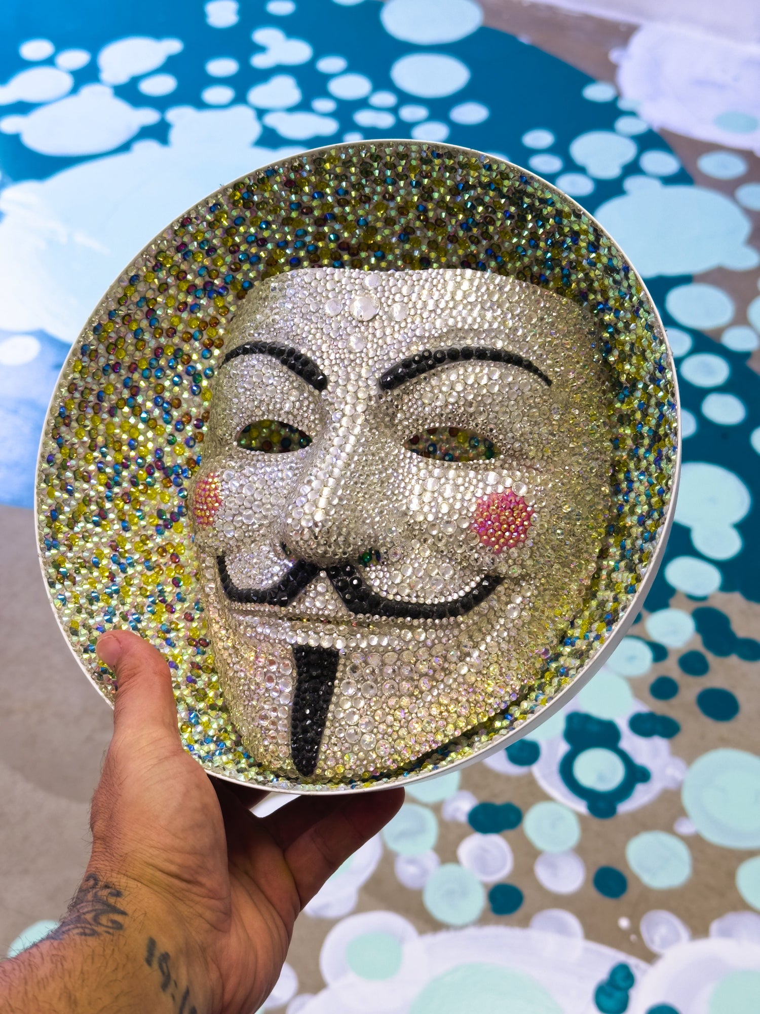 Decorative plate with a face design held by a hand against a patterned background